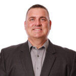 Jeff-01 - AMAA Smiling middle-aged man in a gray suit jacket and light gray shirt, looking at the camera (professional headshot).